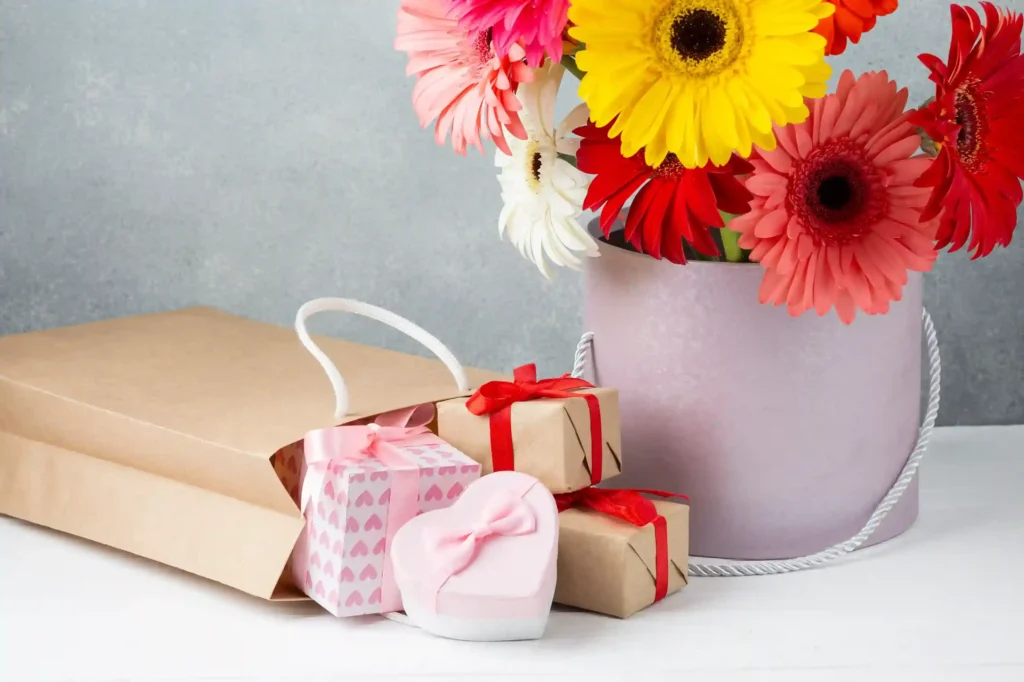Vaso com flores coloridas ao lado de caixas de presente decoradas, simbolizando itens com apelo emocional para o Dia das Mães