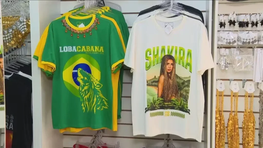 Camisetas temáticas do show da Shakira Rio 2026 expostas em loja, incluindo modelo verde e amarelo com estampa Lobacabana e modelo branco com arte da turnê Las Mujeres Ya No Lloran World Tour