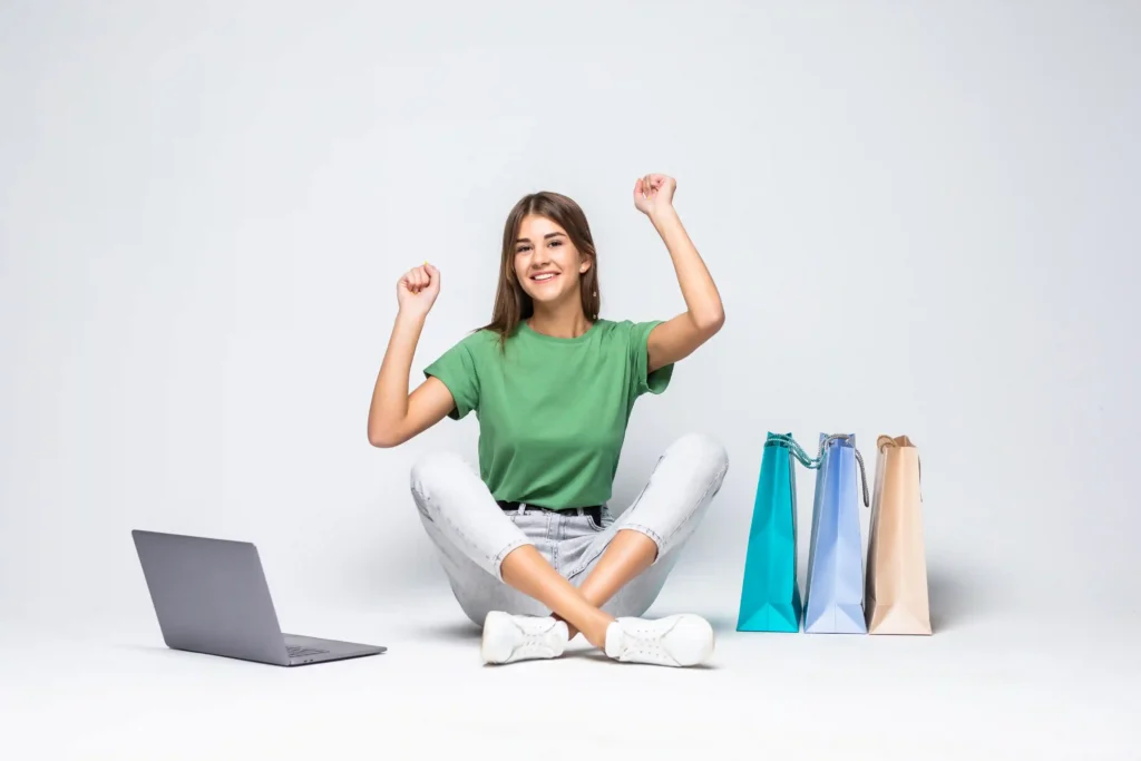 Mulher feliz com compras online ao lado de sacolas e notebook, representando identificação de produtos com potencial após a Páscoa
