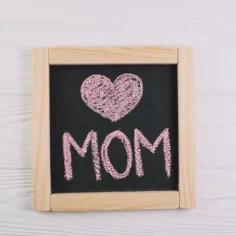 Quadro negro com coração e palavra MOM escritos em giz rosa, representando o encerramento do Dia das Mães e o momento de análise pós-data no Mercado Livre