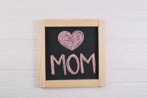 Quadro negro com coração e palavra MOM escritos em giz rosa, representando o encerramento do Dia das Mães e o momento de análise pós-data no Mercado Livre