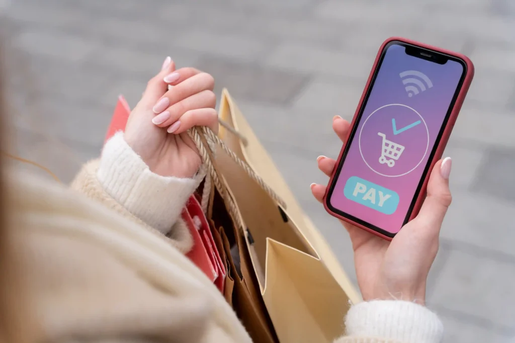 Consumidora com sacolas de compras finalizando pagamento pelo smartphone, ilustrando como otimizar anúncio para celular no Mercado Livre e converter compras pelo smartphone