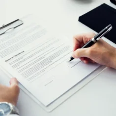 Pessoa assinando documento de termos e condições em prancheta, representando o contrato de adesão do Mercado Livre que todo vendedor aceita ao criar sua conta