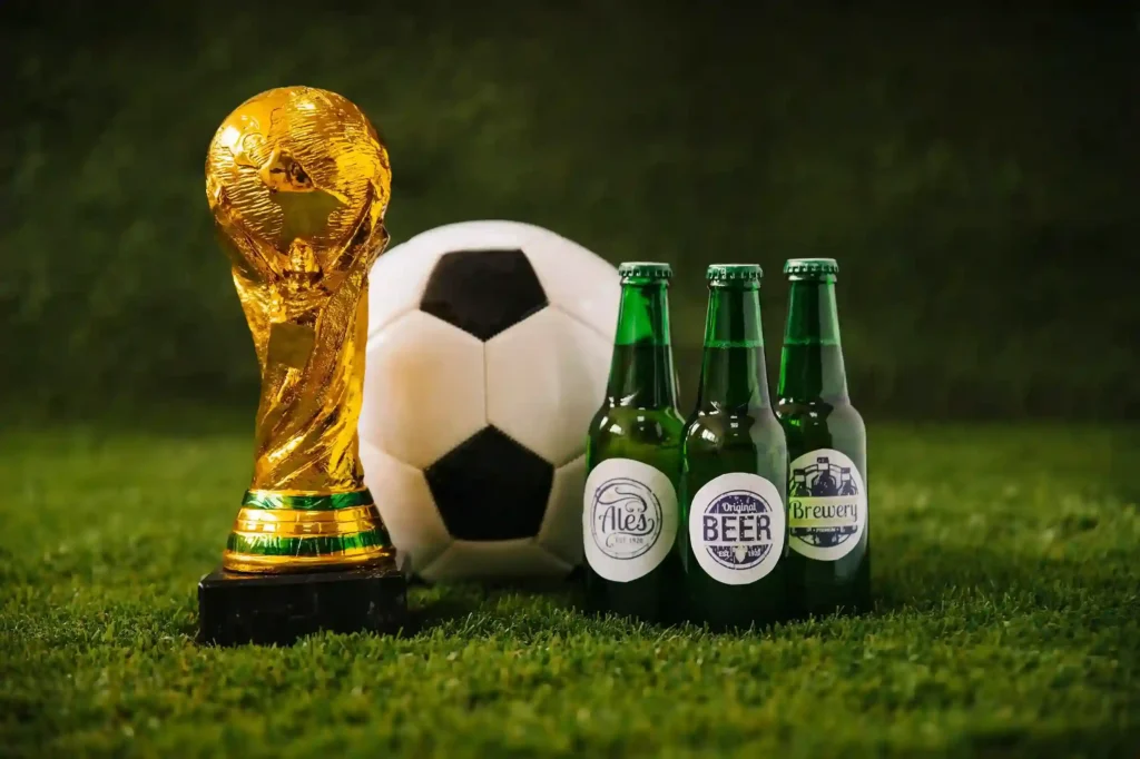 Bola de futebol, garrafas de cerveja, troféu da Copa do Mundo e televisão sobre grama, ilustrando a estratégia de produtos para vender mais no ecommerce durante a Copa 2026