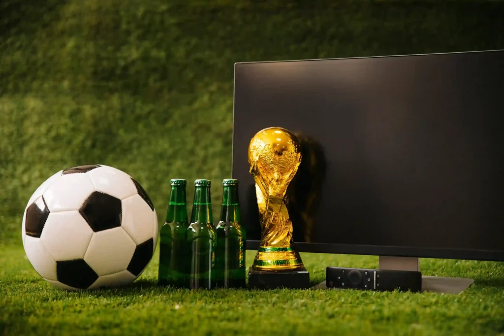 Troféu da Copa do Mundo, bola de futebol e garrafas de cerveja sobre grama, representando os produtos mais vendidos durante os jogos da Copa 2026