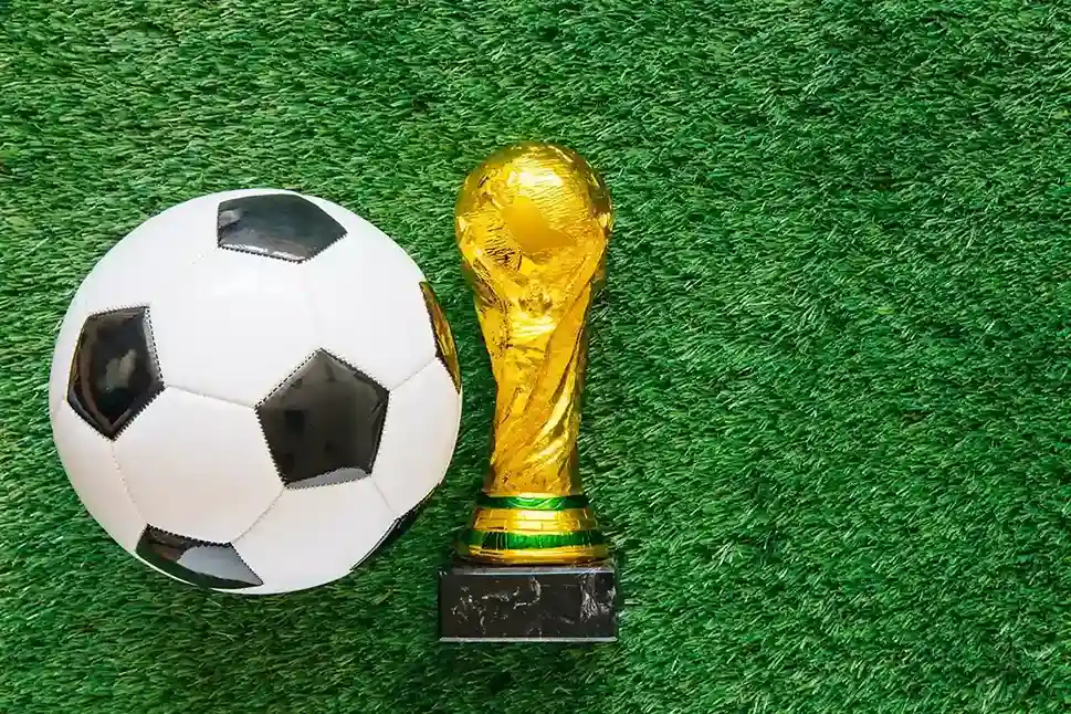 Bola de futebol e troféu dourado sobre gramado verde, ilustrando o comportamento de consumo em casa durante a Copa 2026 e o que vender para aproveitar o momento