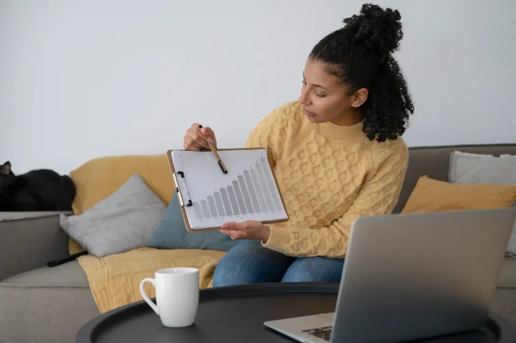 Mulher analisando gráfico de crescimento ao lado de notebook em ambiente doméstico