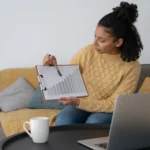 Mulher analisando gráfico de crescimento ao lado de notebook em ambiente doméstico