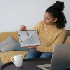 Mulher analisando gráfico de crescimento ao lado de notebook em ambiente doméstico