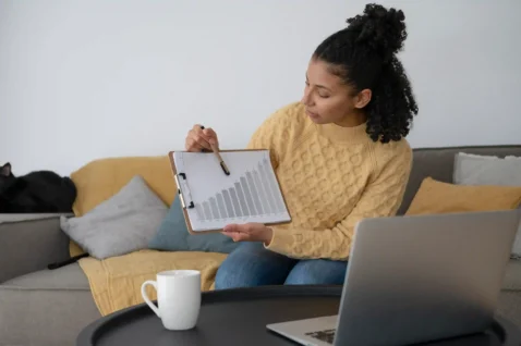 Mulher analisando gráfico de crescimento ao lado de notebook em ambiente doméstico