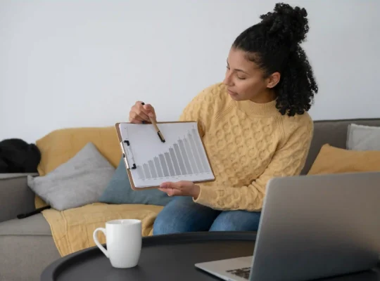 Mulher analisando gráfico de crescimento ao lado de notebook em ambiente doméstico