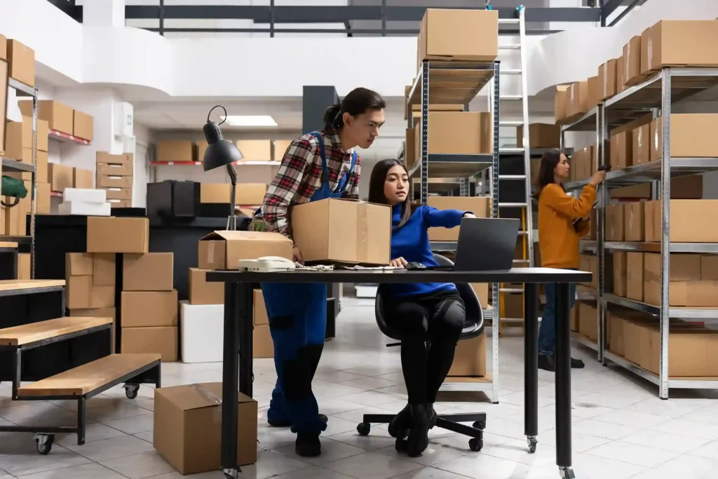 Equipe gerenciando estoque próprio com caixas e notebook em armazém, ilustrando a decisão entre fulfillment próprio ou terceirizado no e-commerce