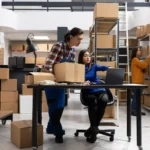 Equipe gerenciando estoque próprio com caixas e notebook em armazém, ilustrando a decisão entre fulfillment próprio ou terceirizado no e-commerce
