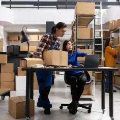 Equipe gerenciando estoque próprio com caixas e notebook em armazém, ilustrando a decisão entre fulfillment próprio ou terceirizado no e-commerce