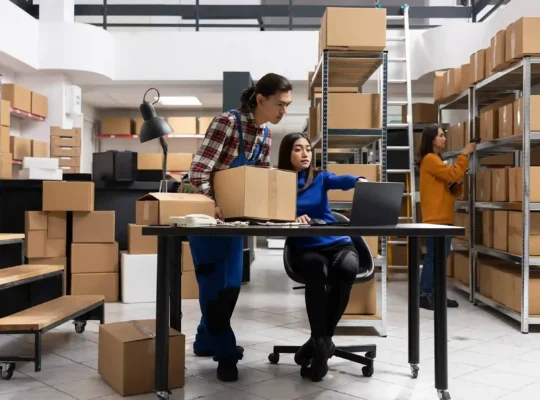 Equipe gerenciando estoque próprio com caixas e notebook em armazém, ilustrando a decisão entre fulfillment próprio ou terceirizado no e-commerce