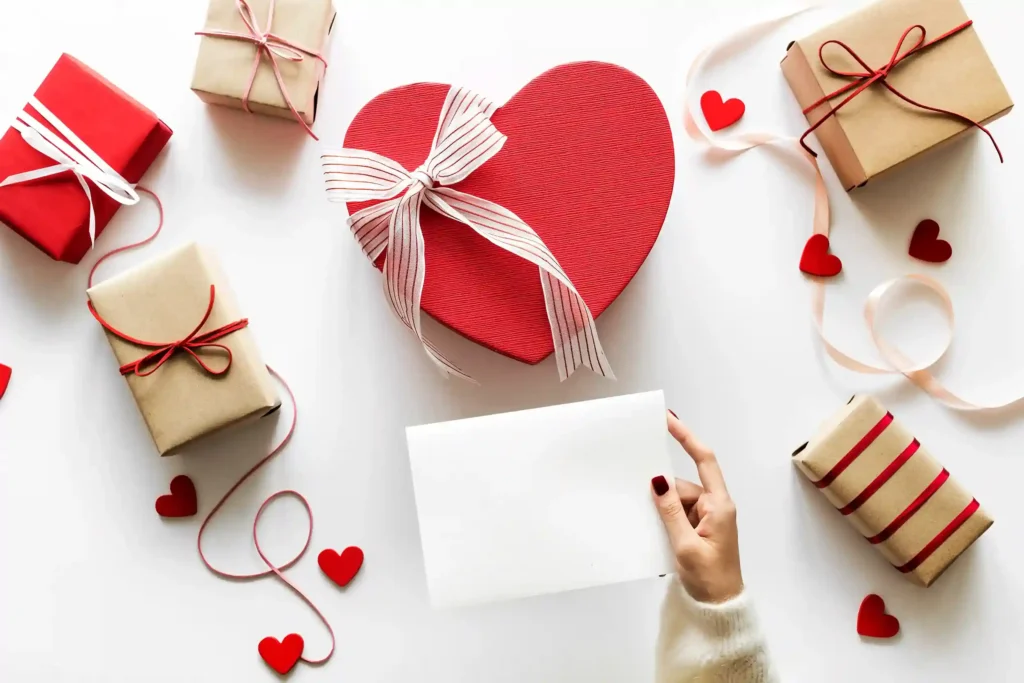Flatlay com caixa coração vermelha, presentes embrulhados e corações decorativos, ilustrando kits do Dia dos Namorados 2026 para vender no e-commerce