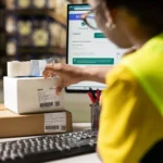 Operadora de logística preparando pacotes com sistema de rastreamento na tela, representando a estratégia de logística no e-commerce em 2026 para sellers no Mercado Livre