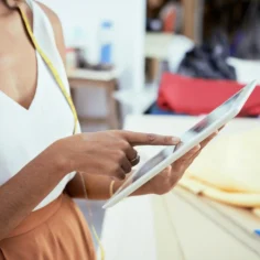 Empreendedora de moda usando tablet com fita métrica no pescoço em ambiente de costura