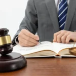 Advogado escrevendo em livro jurídico com martelo e balança da justiça sobre mesa, ilustrando como a LC 214 transforma o marketplace em fiscal do vendedor na reforma tributária