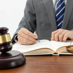 Advogado escrevendo em livro jurídico com martelo e balança da justiça sobre mesa, ilustrando como a LC 214 transforma o marketplace em fiscal do vendedor na reforma tributária