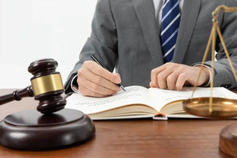 Advogado escrevendo em livro jurídico com martelo e balança da justiça sobre mesa, ilustrando como a LC 214 transforma o marketplace em fiscal do vendedor na reforma tributária