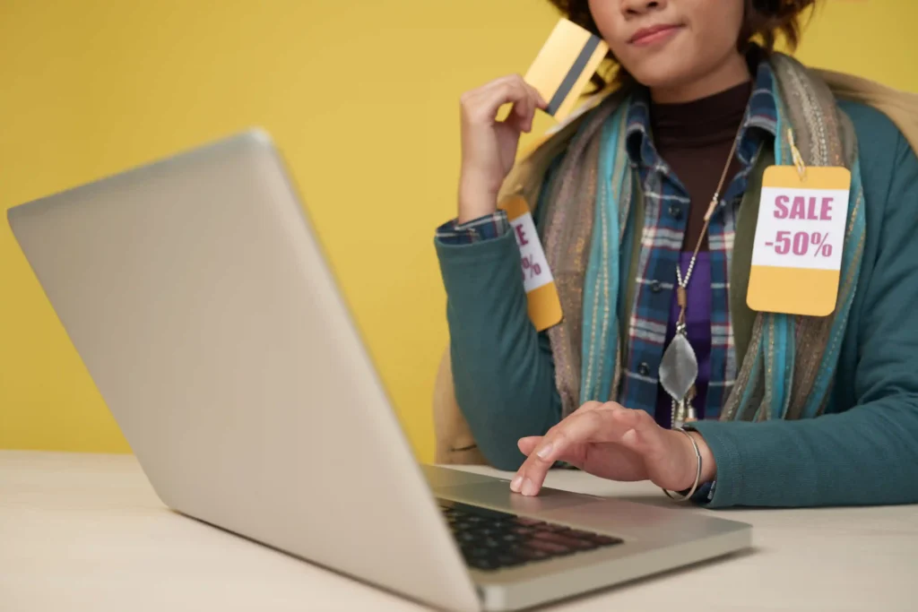 Consumidora com cartão de crédito e etiquetas de desconto navegando no notebook, representando o efeito do parcelamento na conversão e no ticket médio do e-commerce