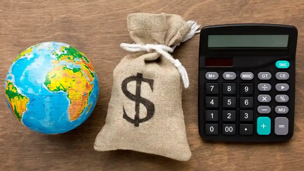 Globo terrestre, saco de dinheiro com símbolo de dólar e calculadora preta sobre mesa de madeira