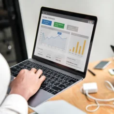 Pessoa digitando em notebook com dashboard analítico exibindo gráficos de vendas e métricas globais na tela