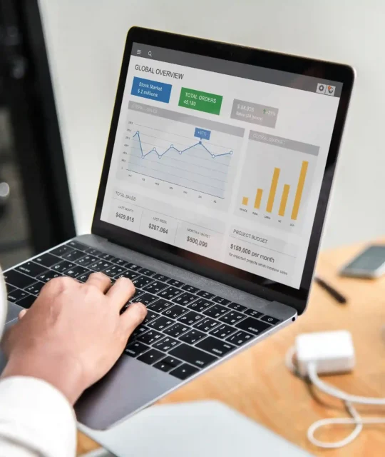 Pessoa digitando em notebook com dashboard analítico exibindo gráficos de vendas e métricas globais na tela