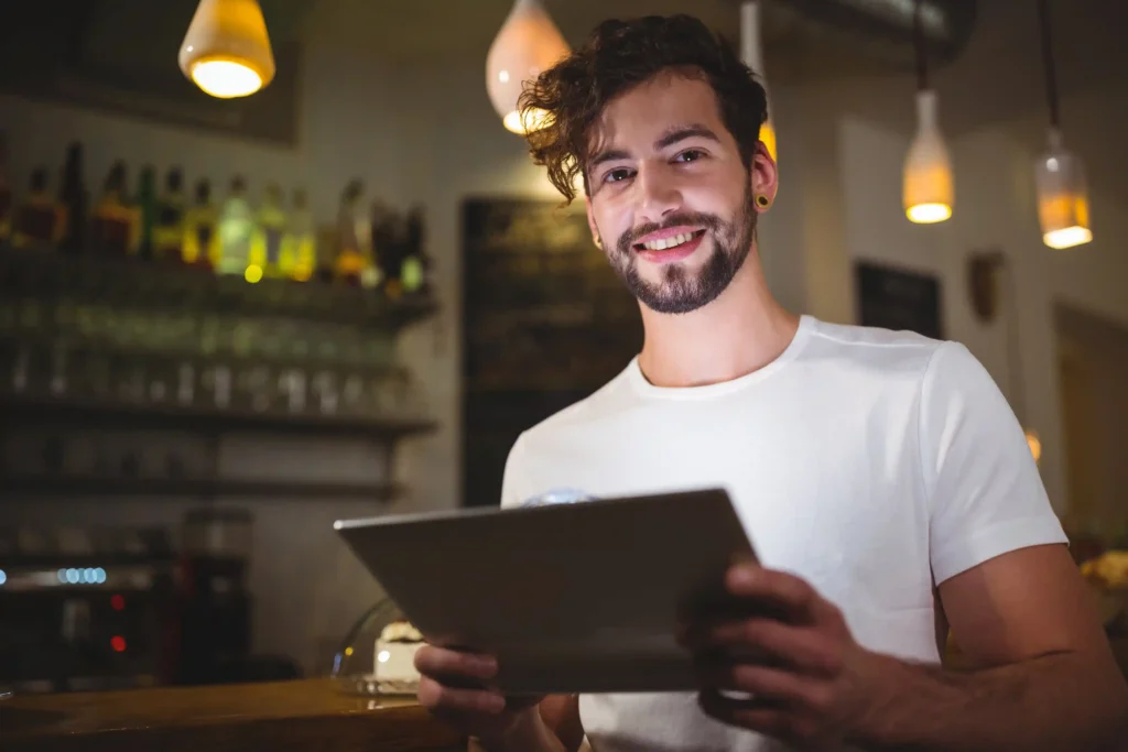 Homem sorrindo segurando um tablet em um estabelecimento comercial, representando um pequeno empreendedor