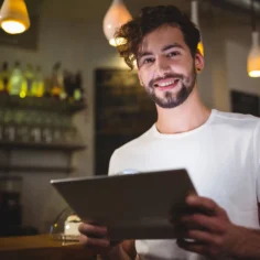 Homem sorrindo segurando um tablet em um estabelecimento comercial, representando um pequeno empreendedor