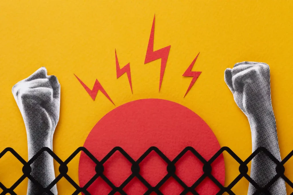 Ilustração com um círculo vermelho atrás de uma cerca preta e dois punhos cerrados nas laterais, além de raios vermelhos que simbolizam restrição ou bloqueio
