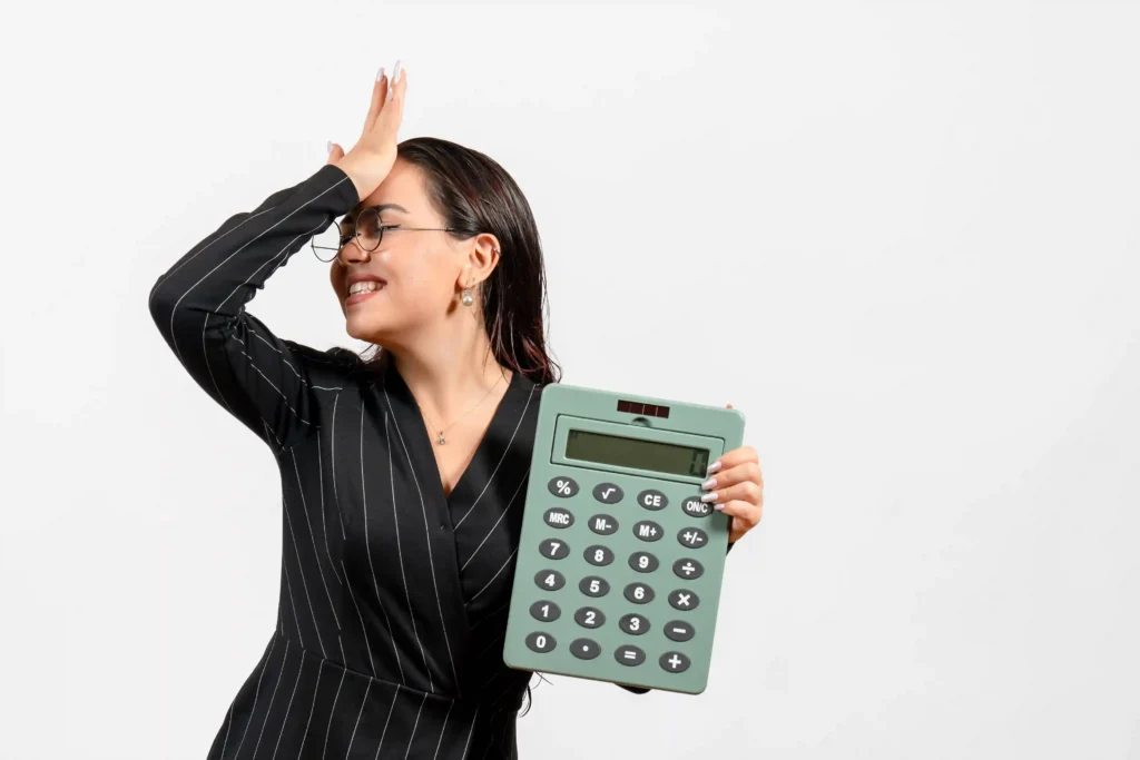 Mulher de terno preto com óculos segurando calculadora grande com expressão de preocupação, fundo branco