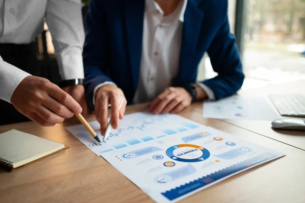 Duas pessoas analisando relatório com gráficos e infográfico financeiro sobre mesa de escritório
