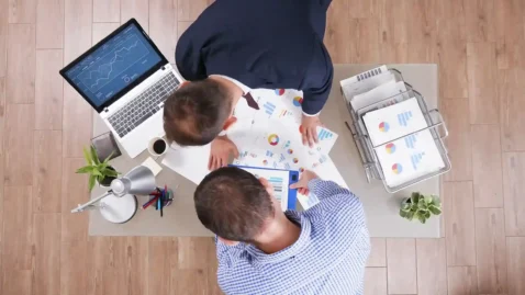 Equipe reunida analisando gráficos e relatórios de vendas em uma mesa de trabalho