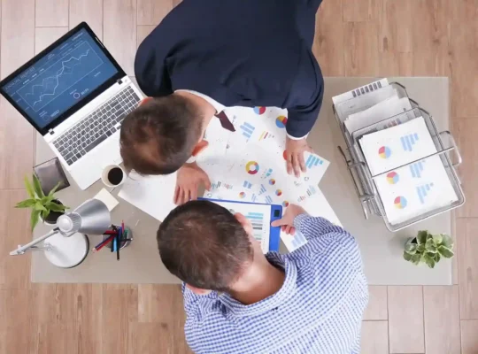Equipe reunida analisando gráficos e relatórios de vendas em uma mesa de trabalho