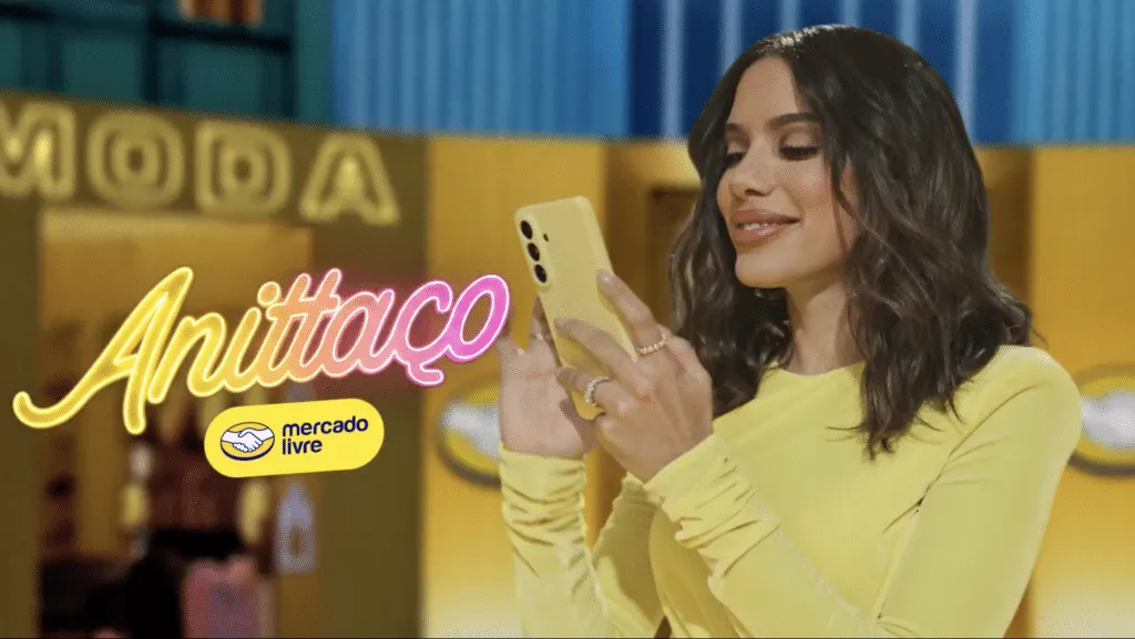 Frame de campanha publicitária Anittaço do Mercado Livre com celebridade de roupa amarela usando smartphone, letreiro "Moda" ao fundo