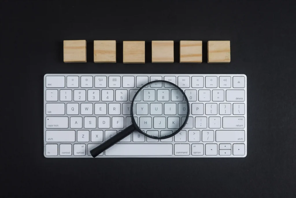 Lupa sobre teclado branco com blocos de madeira enfileirados ao fundo, sobre superfície preta