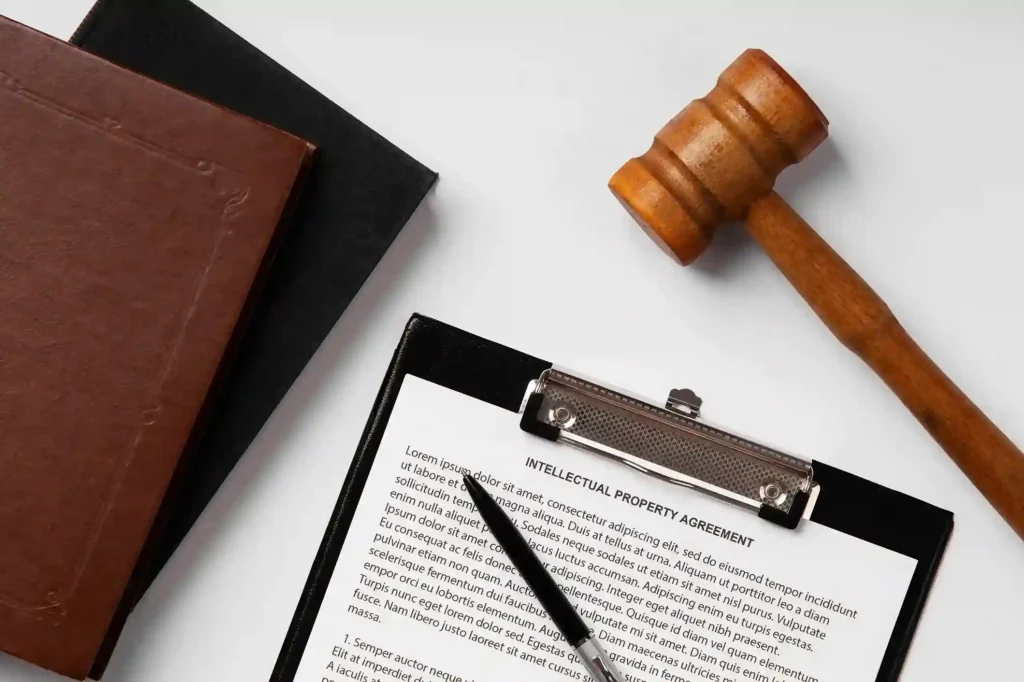 Prancheta com documento intitulado "Intellectual Property Agreement", martelo de juiz e livros jurídicos sobre superfície branca