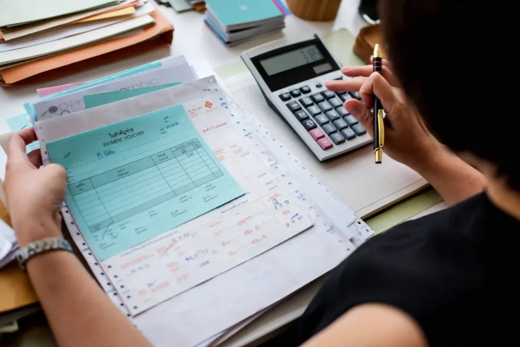 Pessoa conferindo comprovantes de pagamento e calculadora sobre a mesa, ilustrando o controle de dados exigido pela reforma tributária no e-commerce