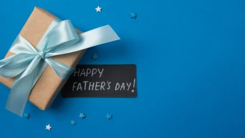Presente embrulhado em papel kraft com laço azul claro e cartão escrito "Happy Father's Day" sobre fundo azul com estrelinhas decorativas