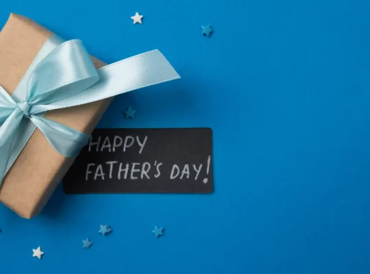 Presente embrulhado em papel kraft com laço azul claro e cartão escrito "Happy Father's Day" sobre fundo azul com estrelinhas decorativas