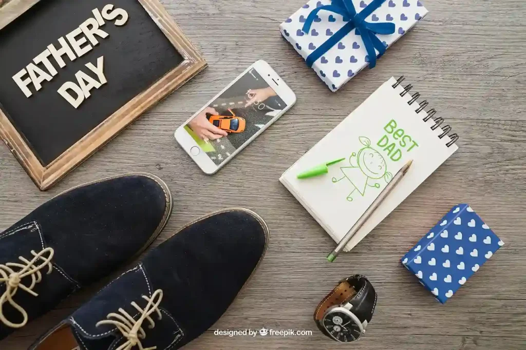 Composição flat lay com sapatos masculinos, relógio, smartphone, presentes embrulhados e caderno com texto "Best Dad" sobre mesa de madeira