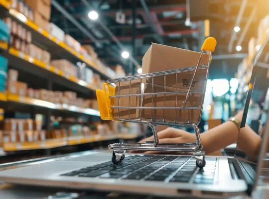 Carrinho de compras em miniatura sobre notebook em ambiente de centro de distribuição, representando a Logística Mercado Livre 2026
