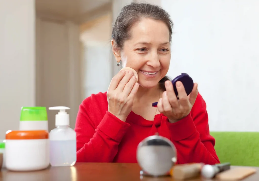 Mulher 45+ aplicando produto de cuidado com a pele madura em frente ao espelho, cercada por potes de creme