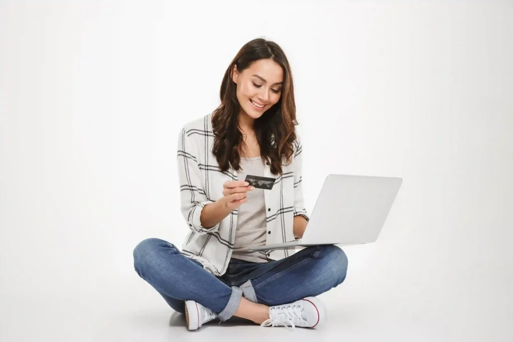 Mulher sentada no chão usando notebook e cartão de crédito para comprar online, refletindo a migração do consumidor em meio ao varejo em queda 2026