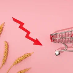 Seta vermelha em queda ao lado de carrinho de compras vazio e espigas de trigo, ilustrando o varejo em queda 2026