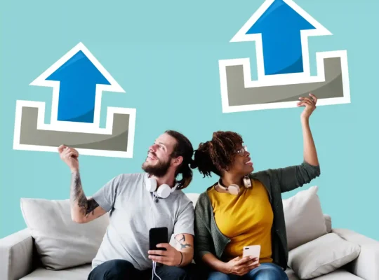 Homem e mulher sentados em um sofá seguram celulares e grandes setas azuis apontadas para cima