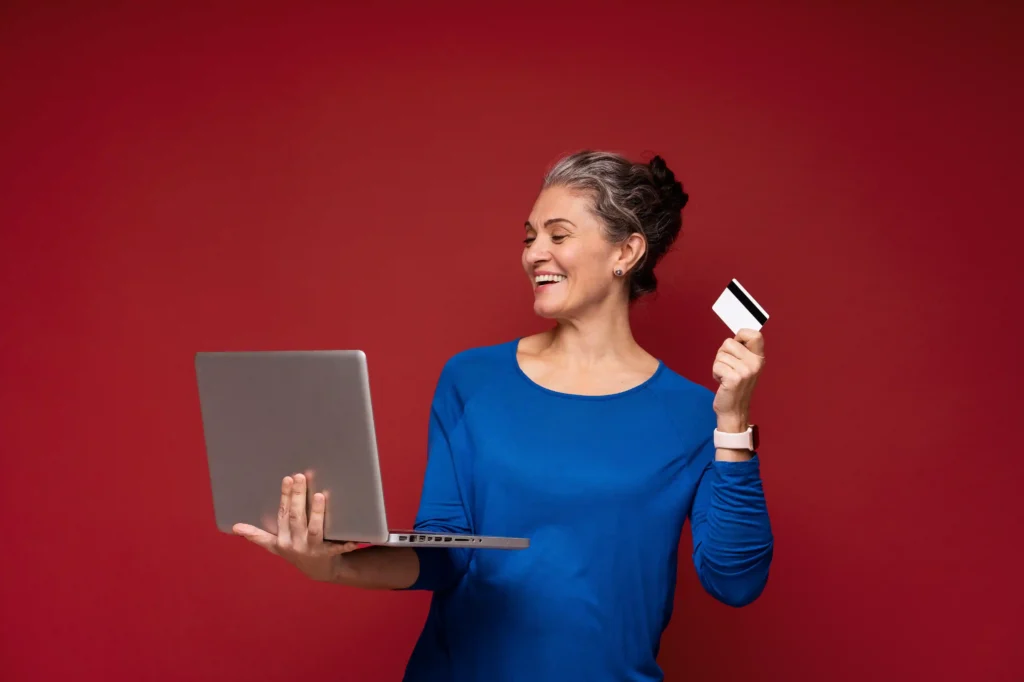 Consumidora 50+ usando notebook e cartão para fazer compras online