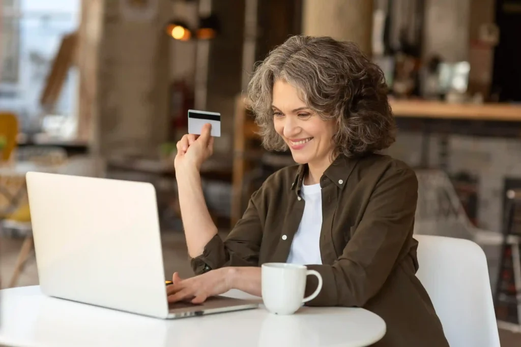Consumidora 50+ fazendo compra pela internet com notebook e cartão